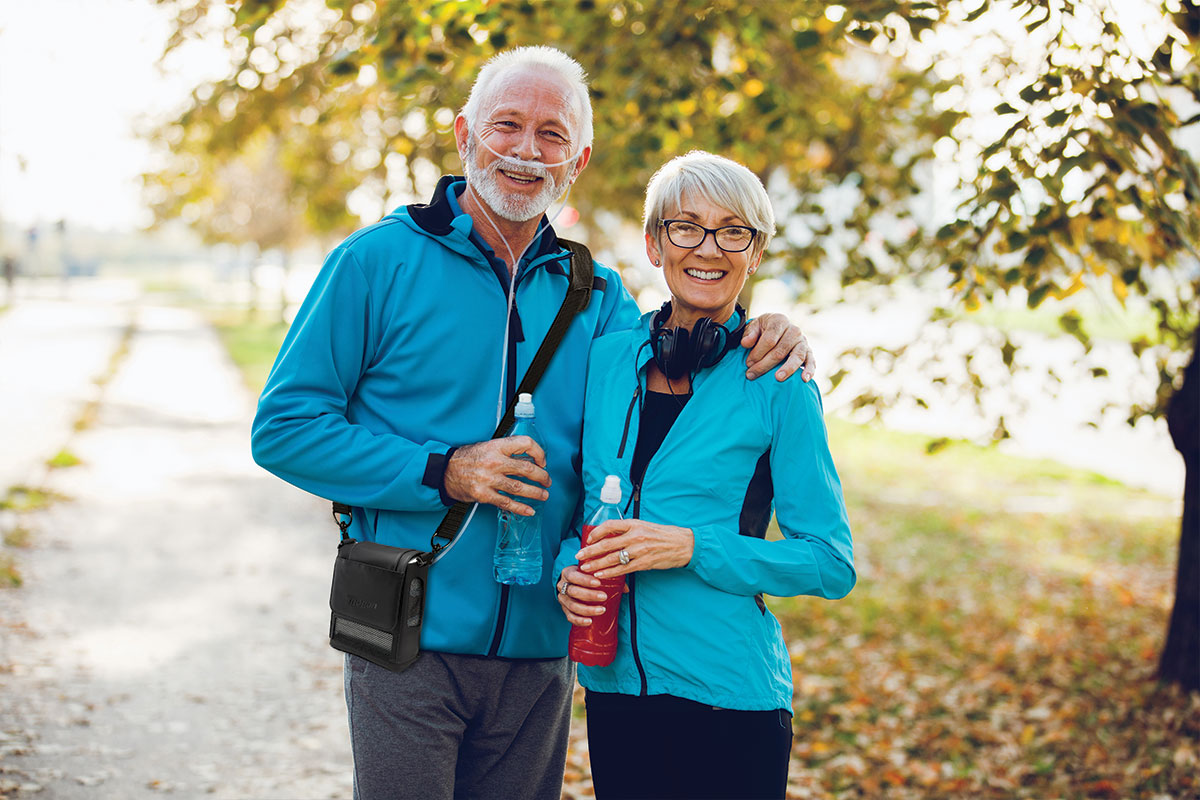 Older couple with oxygen machine smiling in a park